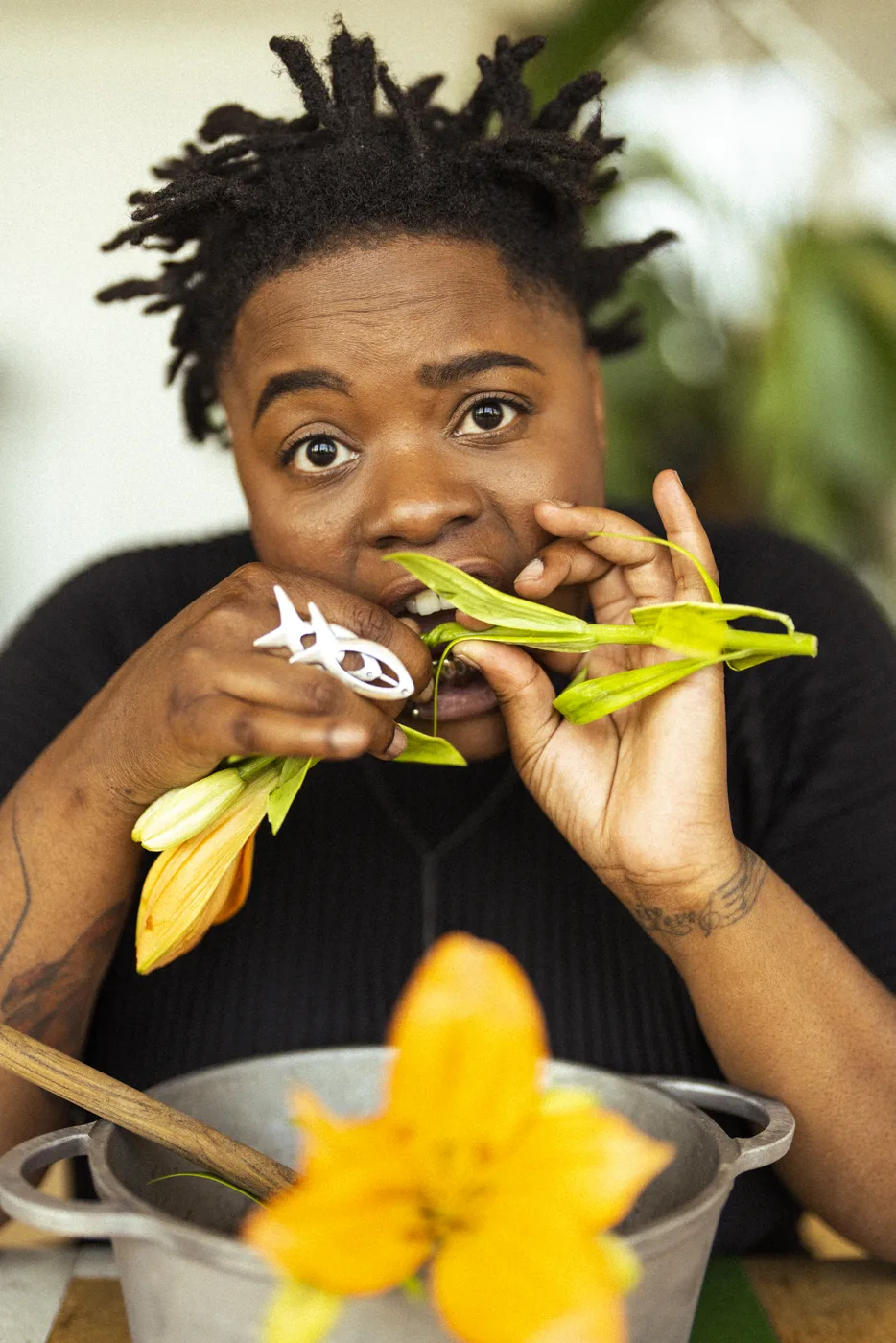Speech Debelle biting a lily stem beside a cooking pot and orange lilies